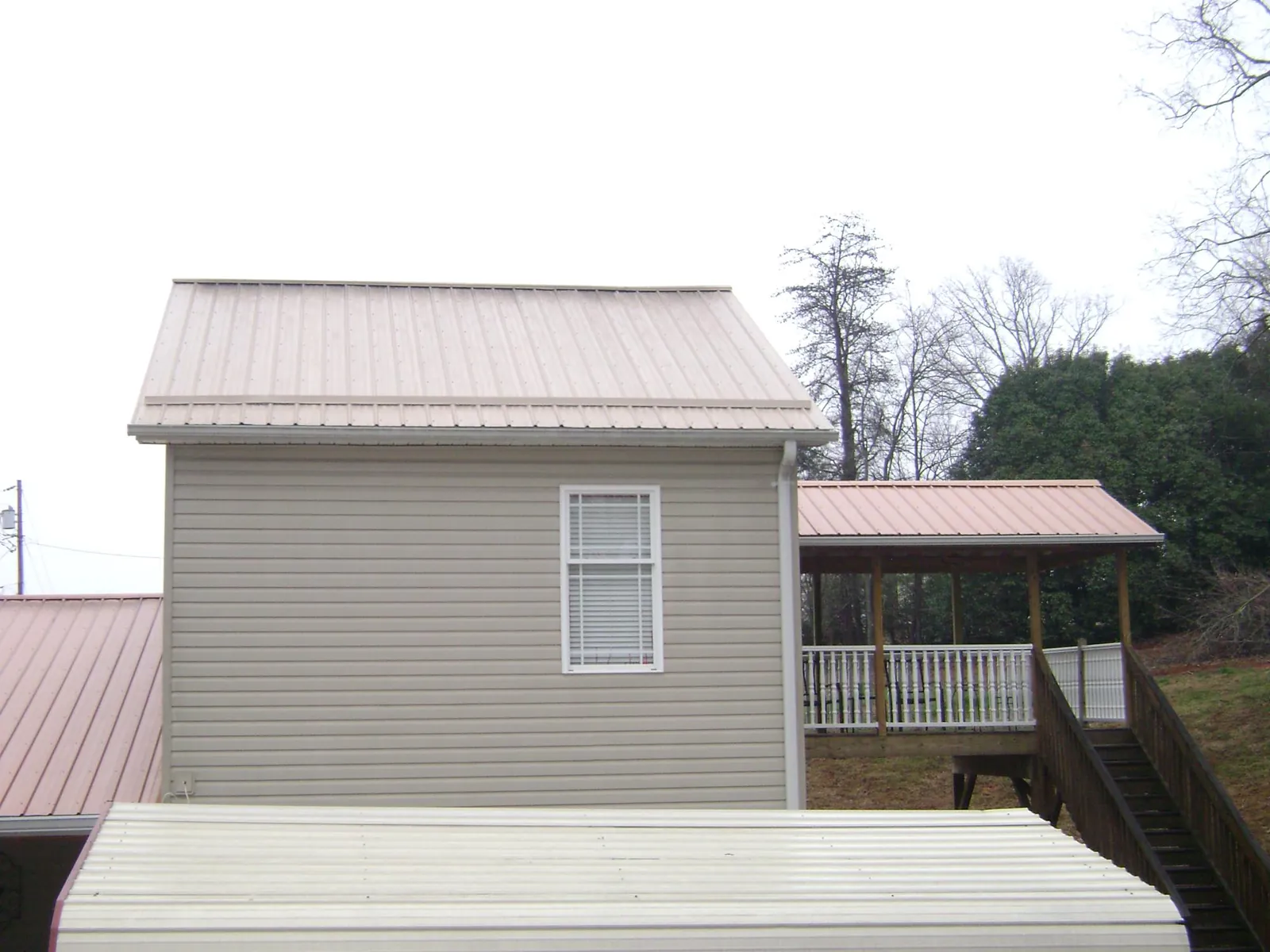 Tan metal roofs on a two story addition and attached porch, from a Roof Replacement job in Rochester